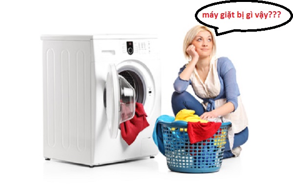 A young woman in thoughts with clothes seated next to a washing machine isolated on white background